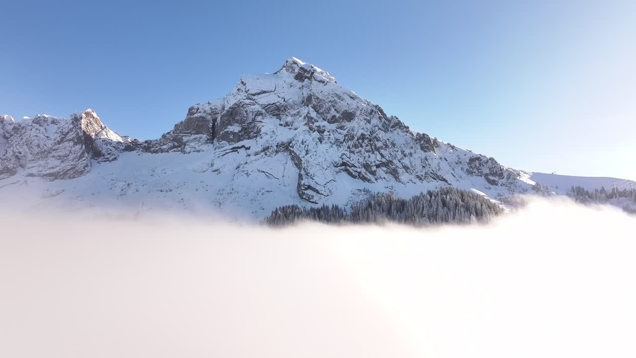 Stunning drone flight over Fronalpstock in Glarus, Switzerland, snowy alpine peaks rise above winter cloud layers, serene beauty of Swiss Alps.