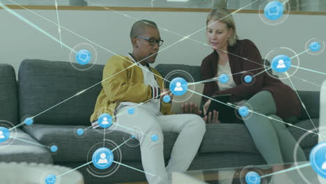 animation of network of connections with icons over diverse colleagues using tablet in office