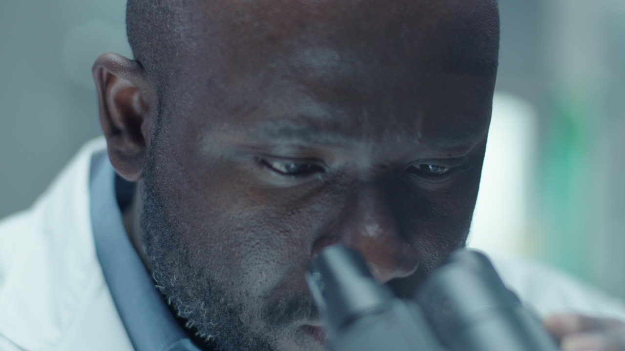 Scienziato afroamericano che osserva al microscopio in un laboratorio medico