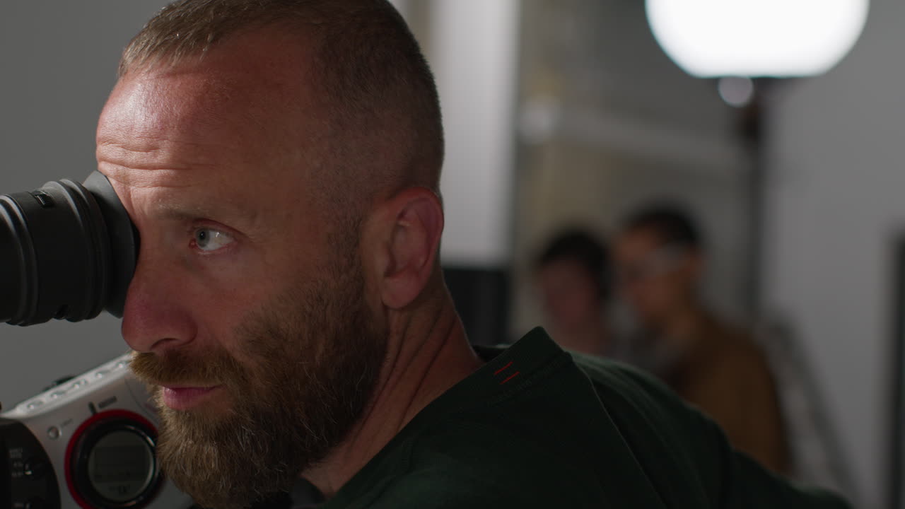primer plano de un operador de cámara de cine masculino mirando a través de un ocular filmando o grabando video en el estudio 2