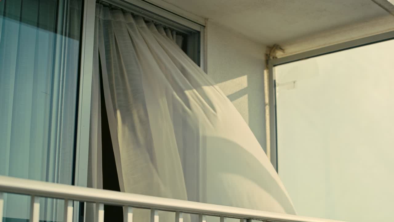 Una tenda bianca trasparente ondeggia verso l'esterno sulla ringhiera del balcone, mentre la brezza solleva e poi adagia il tessuto.