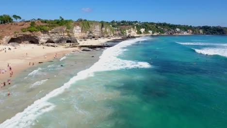 volando sobre surfistas en el agua en la hermosa playa tropical de uluwatu en bali indonesia, vista aérea tomada con drones en 4k, majestuosos acantilados de uluwatu