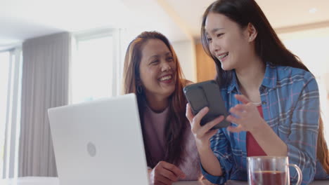 using smartphone and laptop, asian mother and daughter smiling and bonding together