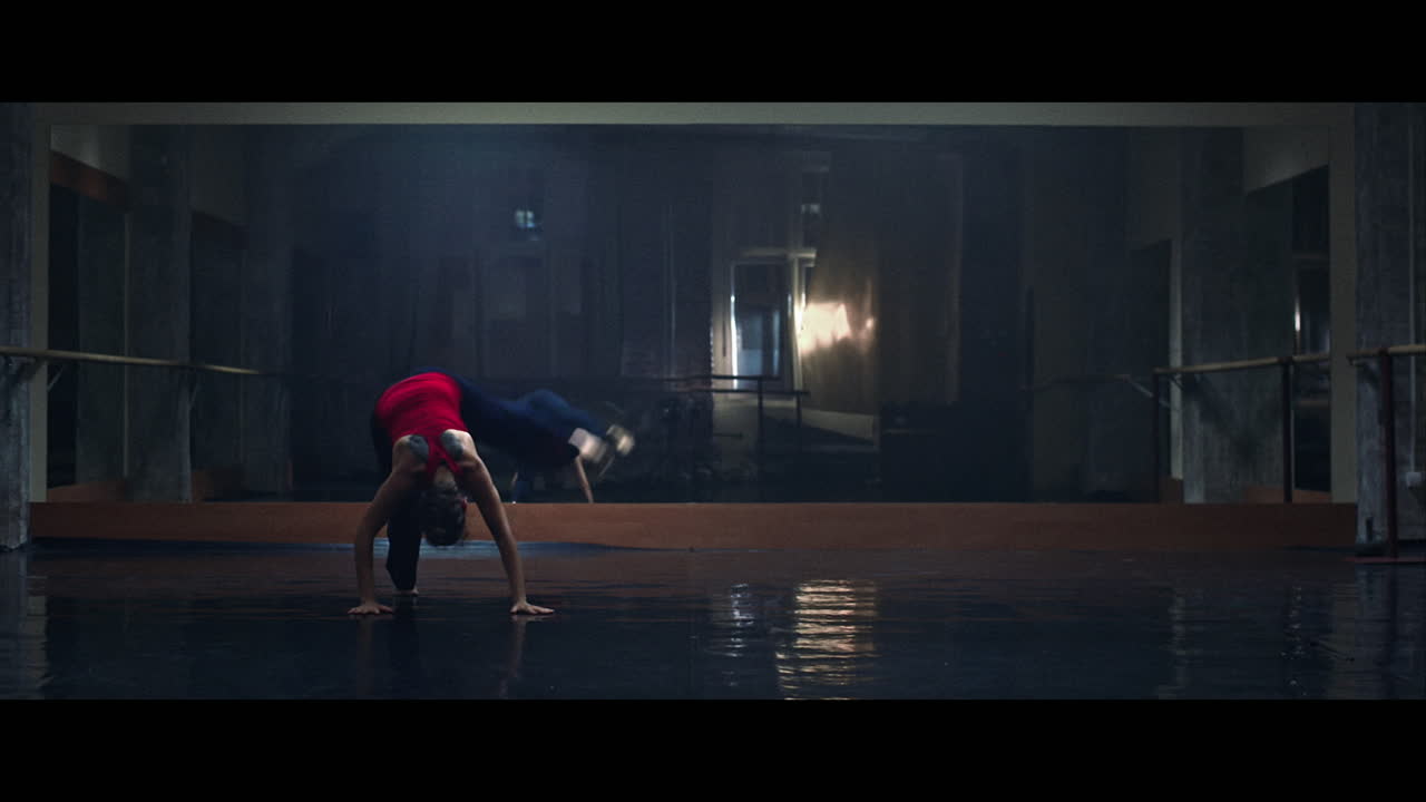 A young woman practices modern dancing and ballet in a moody room full of mirrors