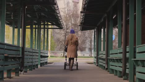 lonely woman walking through empty market while pushing baby stroller, back zoom out view