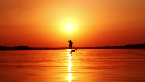 beautiful sunset over the river. man on a sup board approaching camera. low angle view.