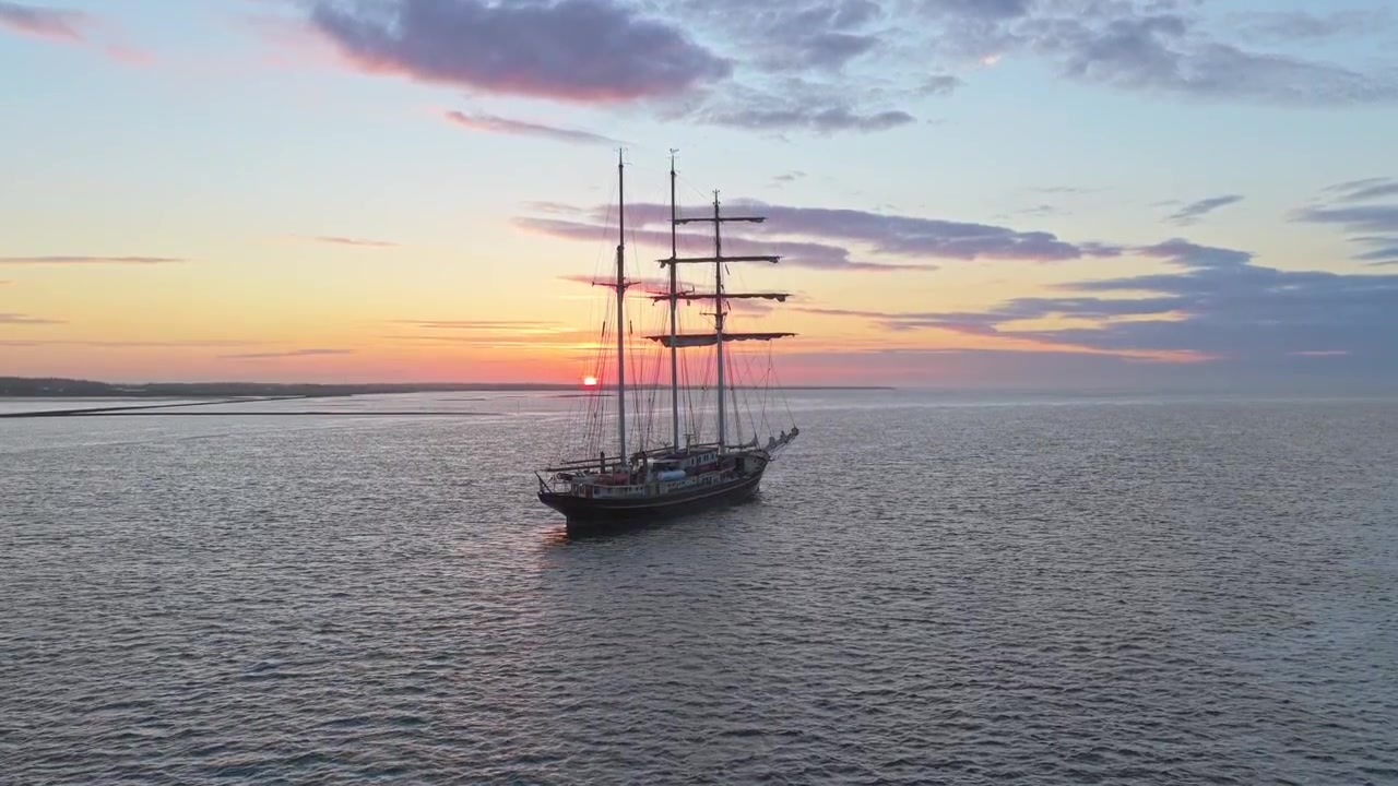 Muhteşem bir gün batımı sırasında Wadden Denizi'nde seyreden görkemli bir yelkenli gemi.