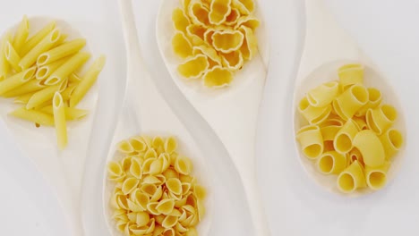 various pasta in wooden spoons on white background