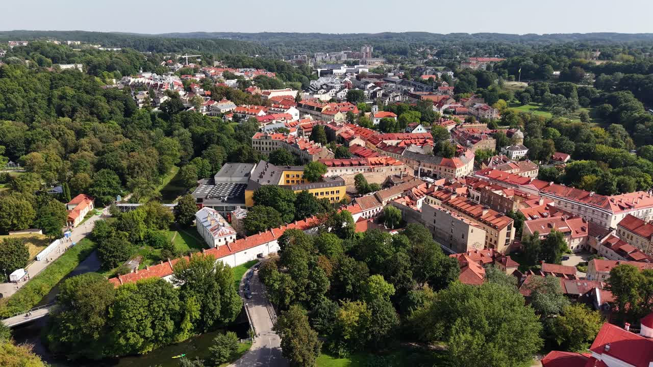 Riprese aeree di volo di un drone sopra il centro storico di Vilnius che mostrano i tetti storici circondati da foreste verdi