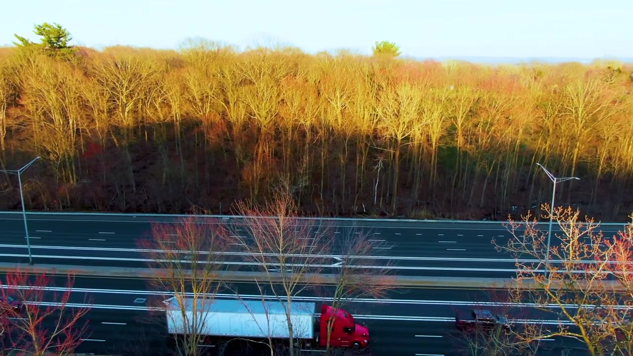 Drone shot panning across a curved highway with moving vehicles surrounded by trees during a spring afternoon in Windsor Connecticut