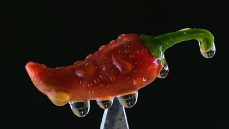 disparo macro extremo de pimienta roja con gotas de agua giratorias pegadas en un cuchillo afilado