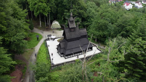 vista aérea lejos de la iglesia de madera en fantoft nublado, noruega - marcha atrás, inclinación, disparo de drones