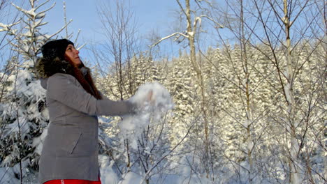 woman tosses handful of snow up into air in front of forest, snow flurries fly