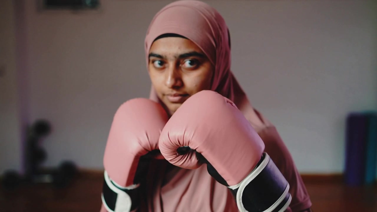 Esercizio di allenamento con donna che indossa un hijab e sferra un jab diretto in una palestra domestica, con guantoni rosa