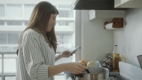 woman texting on phone while cooking meal in the kitchen