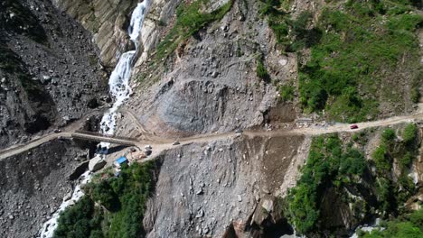 rupse falls and off-road suv cars drive on steep slope mountain dirt road crossing bridge over waterfall in central nepal - aerial dolly