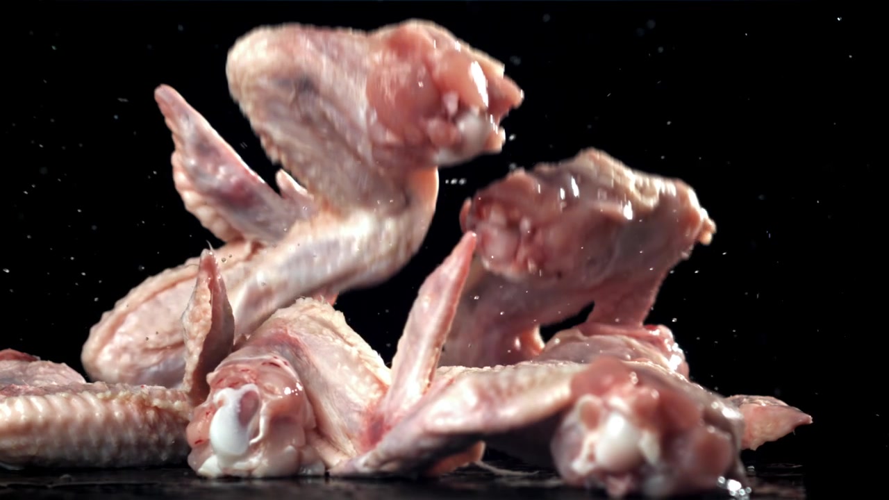 Alitas de pollo crudas cayendo y salpicando agua en cámara lenta
