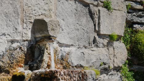 El-Agua-Fluye-De-Un-Viejo-Grifo-En-Un-Muro-De-Piedra