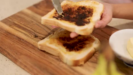hands spreading vegemite on toast slices in a well-lit kitchen environment, showcasing a simple breakfast preparation