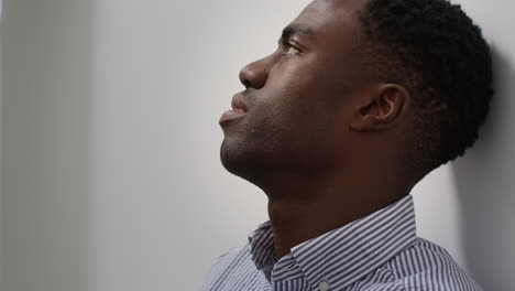 young man with mental health issues standing leaning against wall in office looking depressed and unhappy