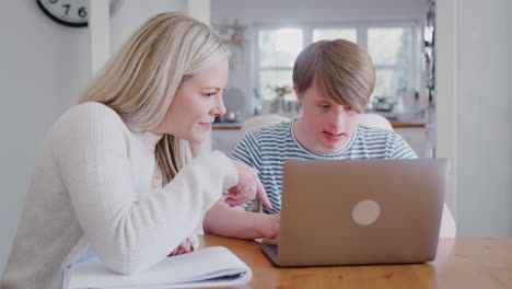 downs syndrome man sitting with female home tutor using laptop for lesson at home