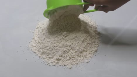 adding the second cup of bread flour by a measuring cup, onto the pile of flour on the white and clean kitchen top