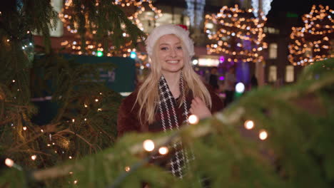 young attractive lady puts on christmas hat whilst stood under a xmas tree