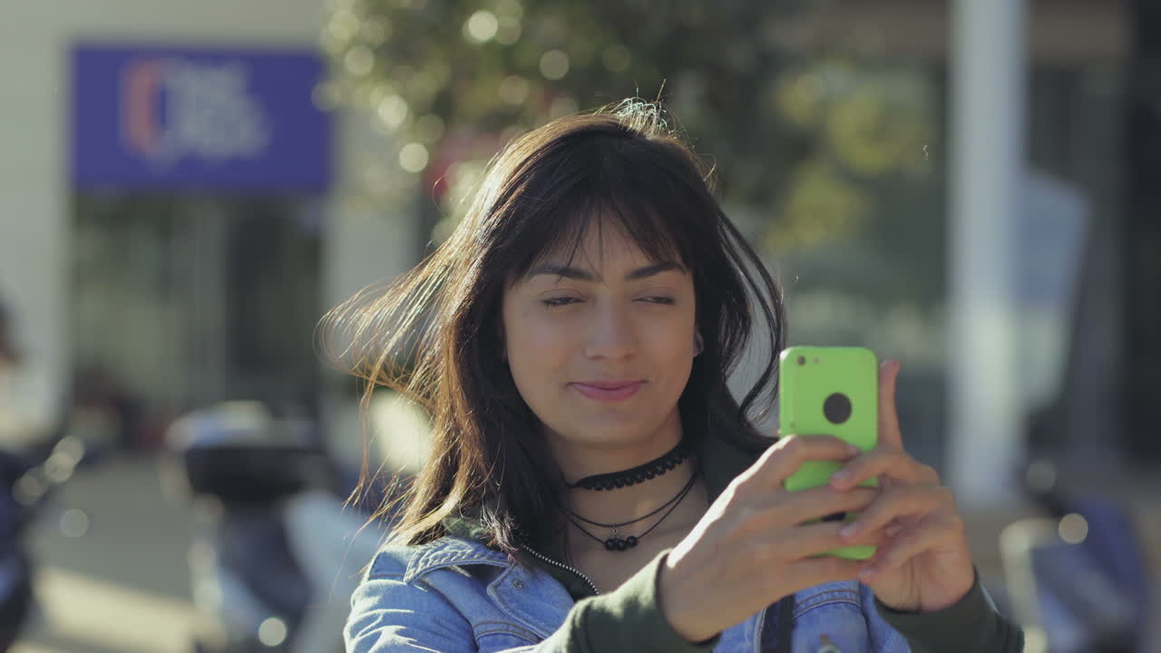 Giovane donna sorridente che scatta foto con lo smartphone all'aperto.