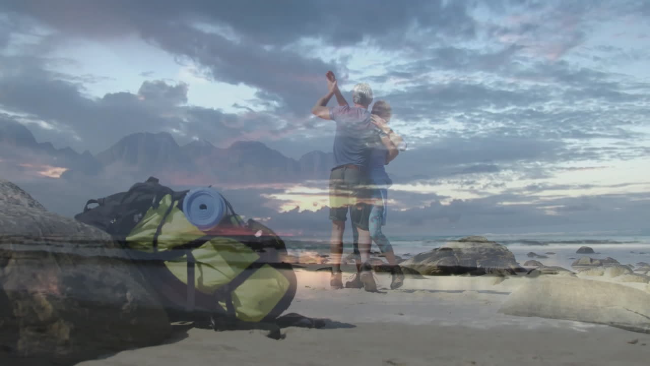 mature man and woman dancing on beach at sunset, displaying animated mountain overlay for travel