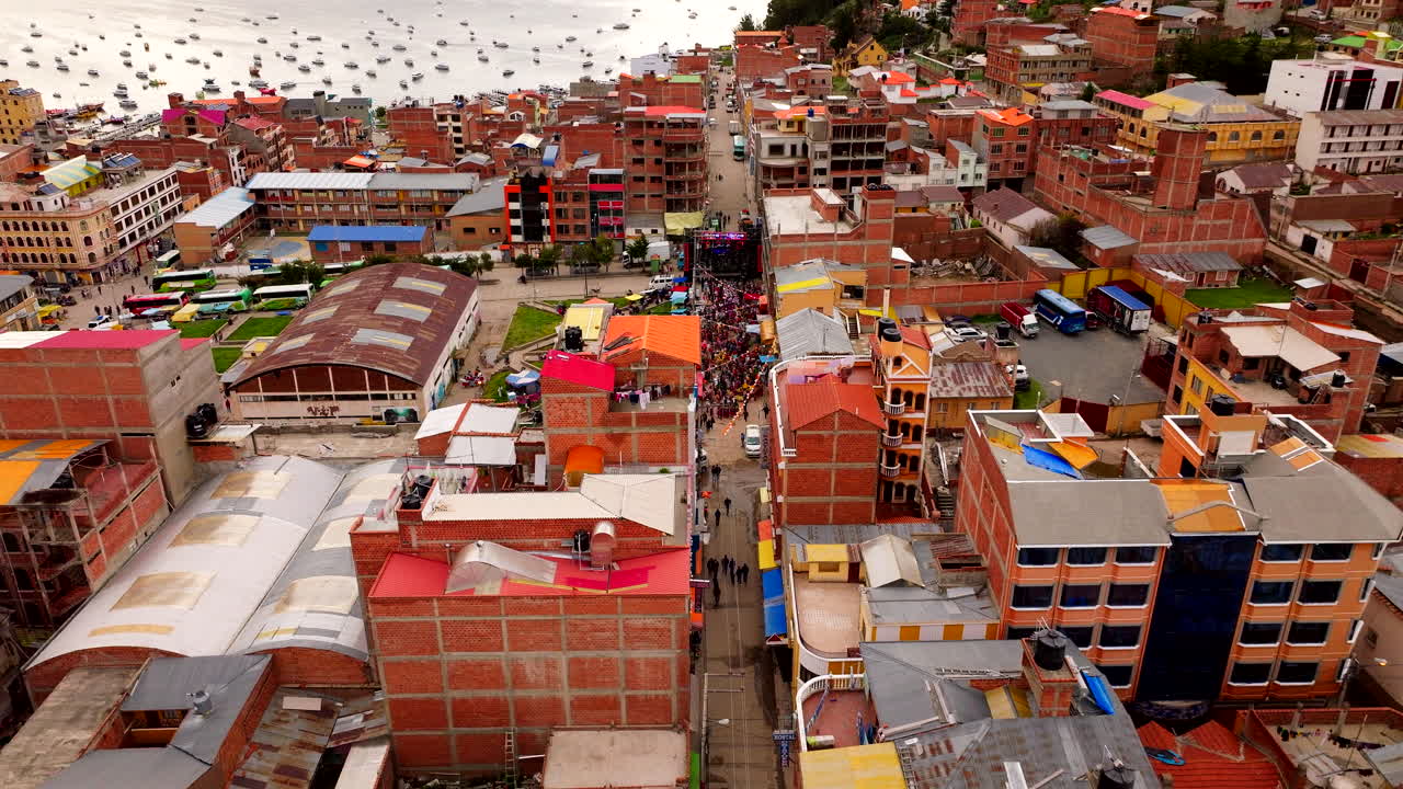 Vista aerea cinematografica di un drone su una vivace parata di Carnevale che si snoda per le strade di Copacabana, Bolivia. La folla colorata è circondata da edifici con il lago Titicaca sullo sfondo.