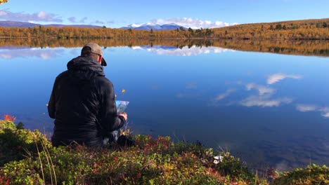 hiker reading his map sitting by the edge of a crisp clear mountain lake during autumn in abisko, lapland, sweden