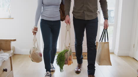 close up of couple returning home from shopping trip carrying groceries in plastic free bags