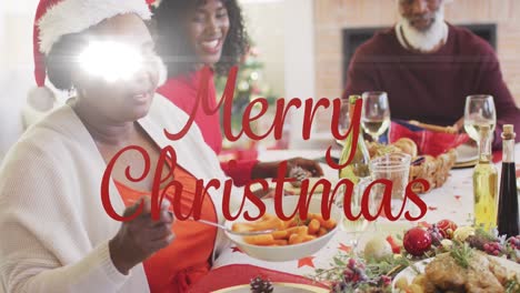 Merry-christmas-text-banner-against-african-american-woman-serving-food-while-having-dinner