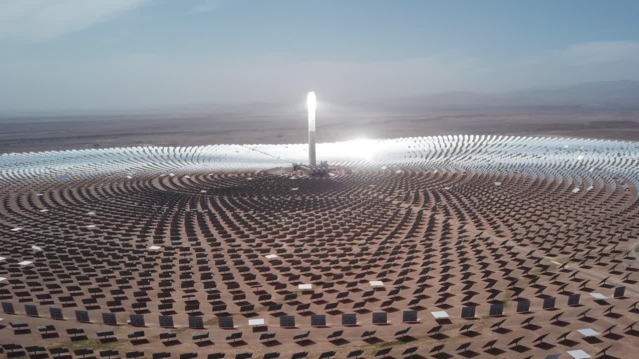 Bredt filmisk etableringsbillede af Noor III solcelleanlægget. Det viser det glødende centrale tårn og et enormt heliostatfelt, der skaber et futuristisk sci-fi landskab i ørkenen.