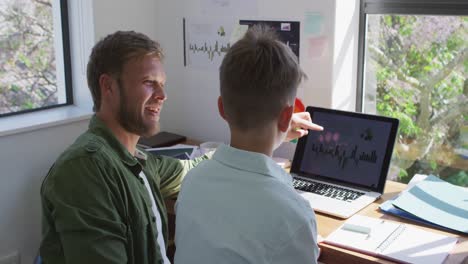 Kaukasischer-Mann-Und-Sein-Sohn-Sitzen-Zu-Hause-An-Einem-Tisch-Und-Benutzen-Einen-Laptop