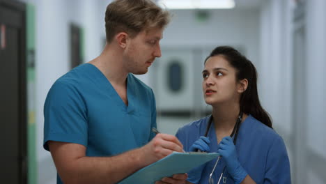 Surgeon-discussing-patient-diagnosis-with-nurse-standing-clinic-corridor-closeup