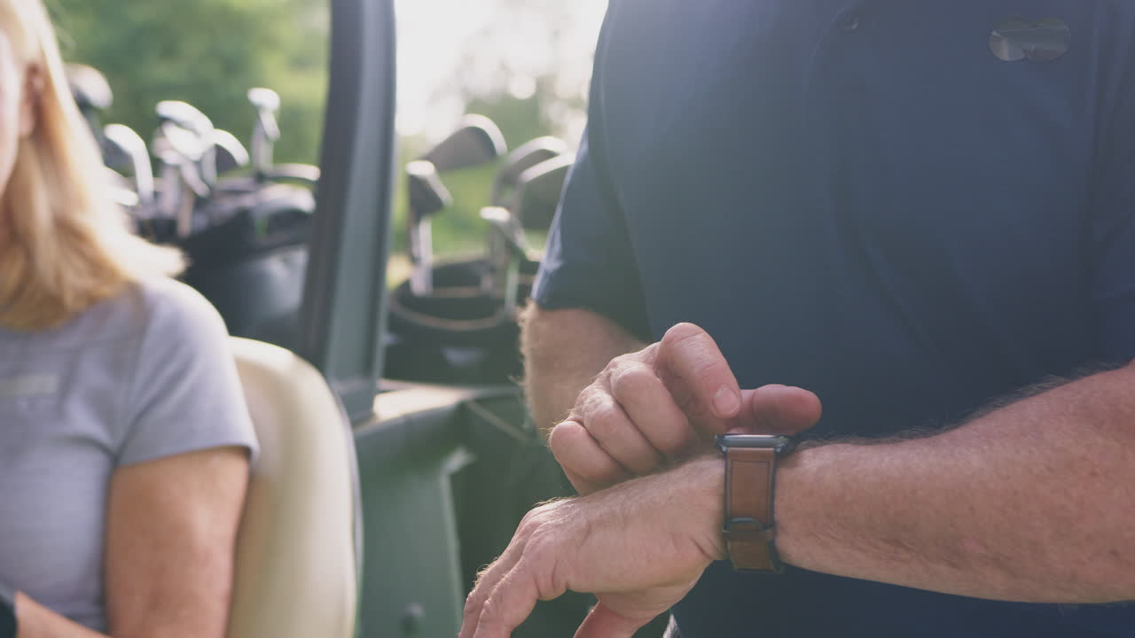 cerca del hombre comprobando reloj inteligente como una pareja madura sentarse en el buggy y jugar una ronda de golf juntos