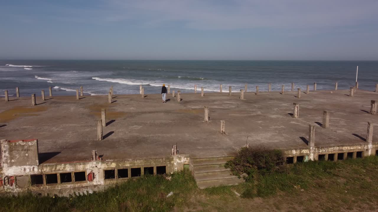 아르헨티나의 황금빛 일몰 동안 멋진 바다 전망을 갖춘 오래된 건물 옥상을 걷는 사람의 공중 궤도 샷