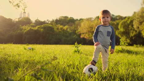 Junge-Steht-Bei-Sonnenuntergang-Mit-Einem-Fußball-Auf-Dem-Gras.