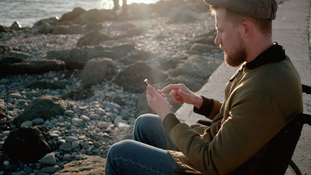 체어 에 앉은 남자 가 해변 에서 전화 를 사용 하고 있다