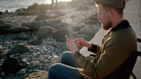 man in wheelchair using phone at the beach