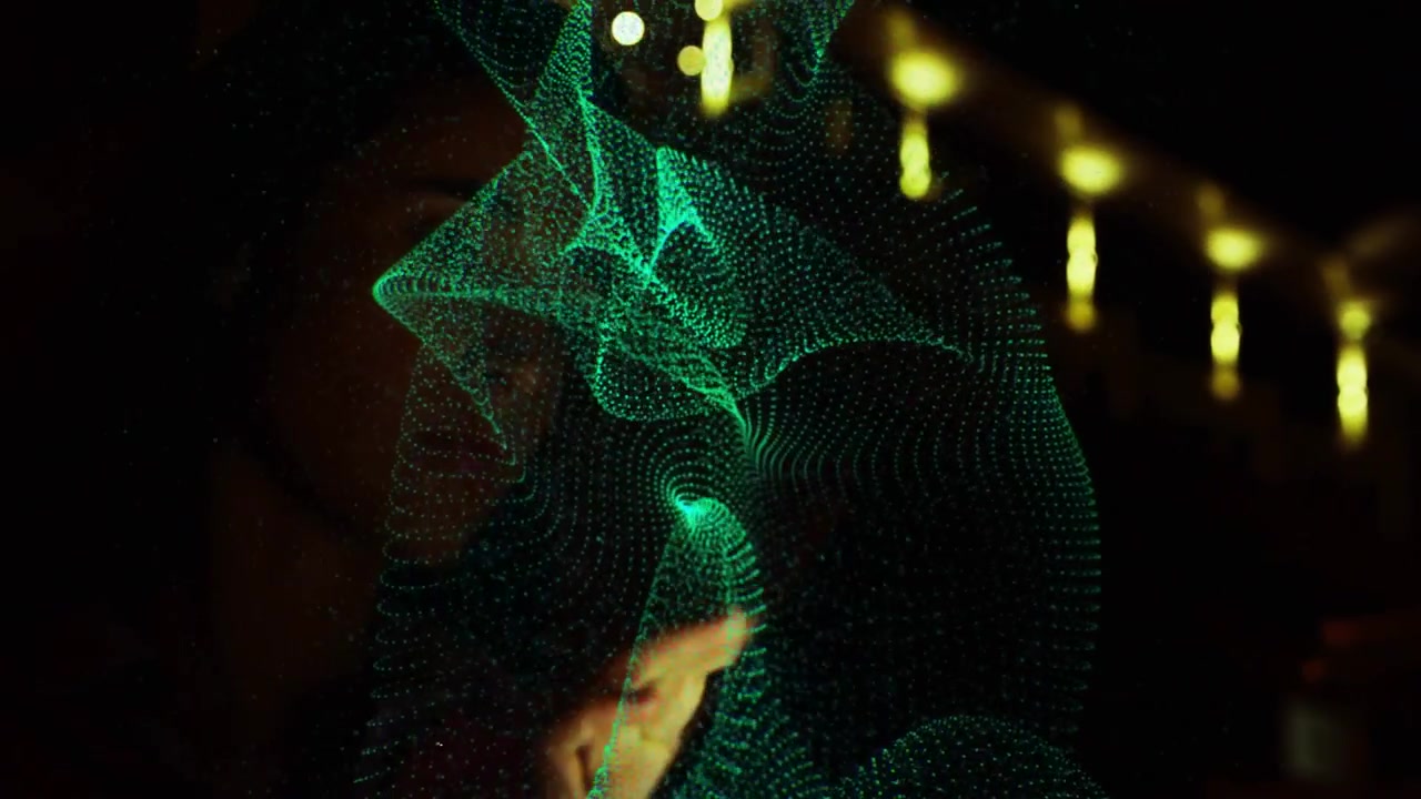 Woman raising finger toward glass panel, causing green holographic mesh shaping in tech demo