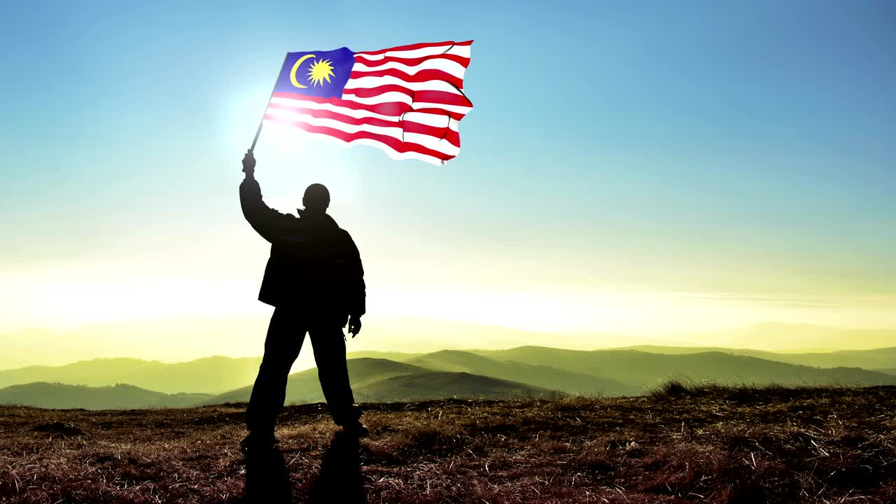 Silhouette di uomo vincitore di successo che sventola la bandiera della Malesia sulla cima della montagna, sfondo Cinemagraph LOOP