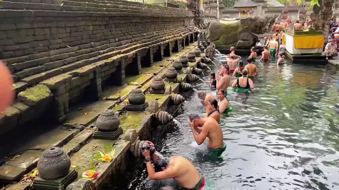 Purification ritual at Tirta temple, traditional spiritual practice, sacred Balinese water blessing as practioners gather in pool and cleanse themselves
