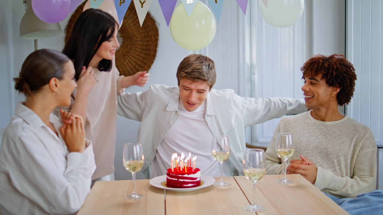 Friends surprising birthday boy bringing cake closeup. Amazed man blowing candle