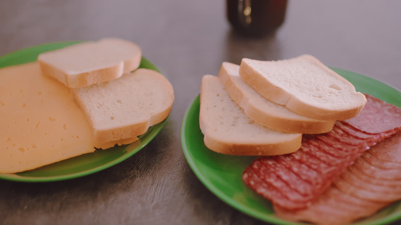 Primo piano di pane affettato impilato con strati di carne su un piatto verde posto su un tavolo con sfondo sfocato che mette in risalto una tazza di caffè caldo, che mostra una semplice composizione per la colazione fatta in casa in un'accogliente cucina