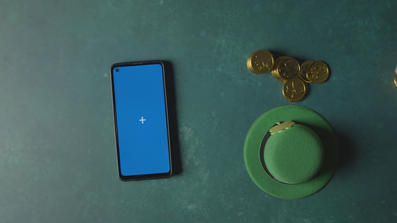 Overhead Studio Shot Of Green Leprechaun Top Hat With Gold Coins And Blue Screen Mobile Phone To Celebrate St Patricks Day 1