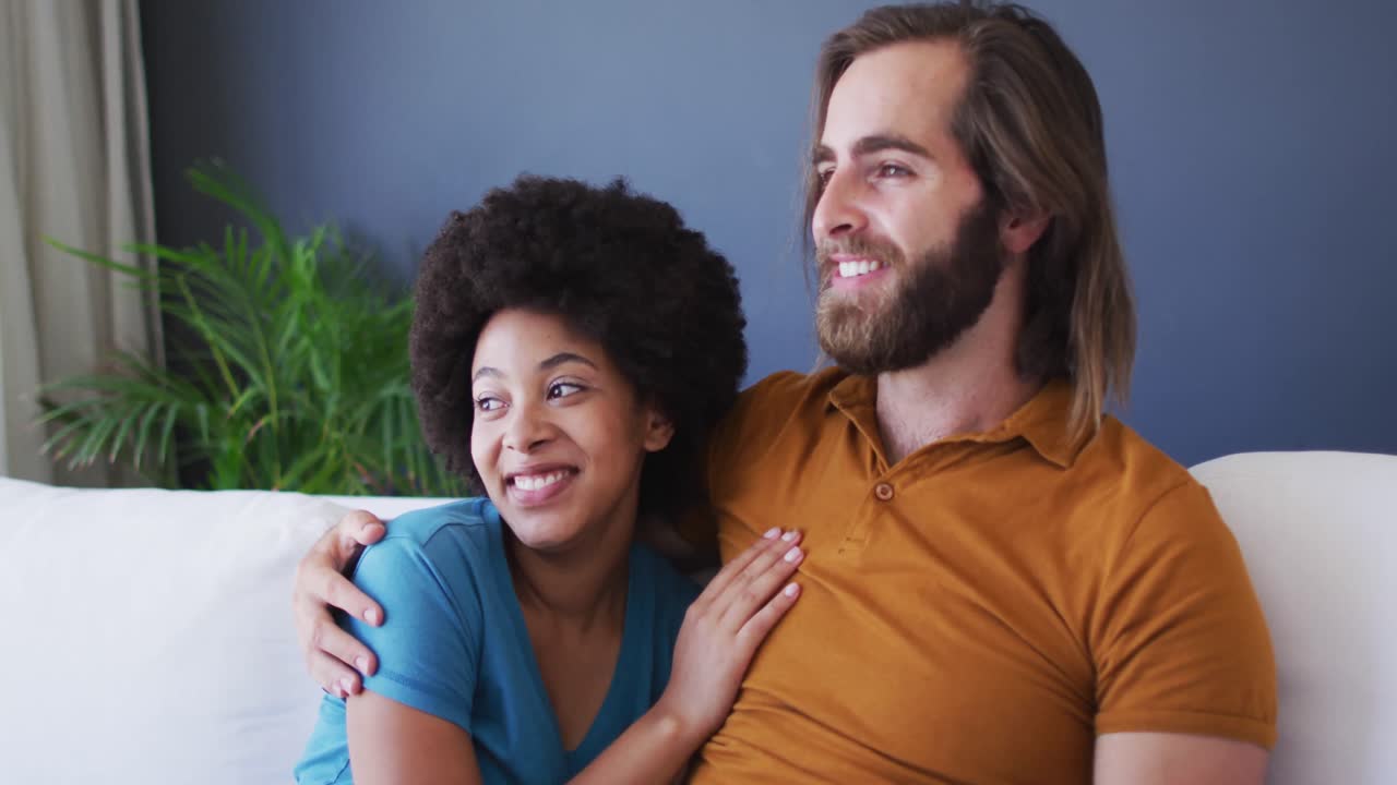 Mixed race couple embracing each other while sitting on the couch at home