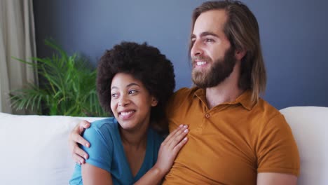 Mixed-race-couple-embracing-each-other-while-sitting-on-the-couch-at-home