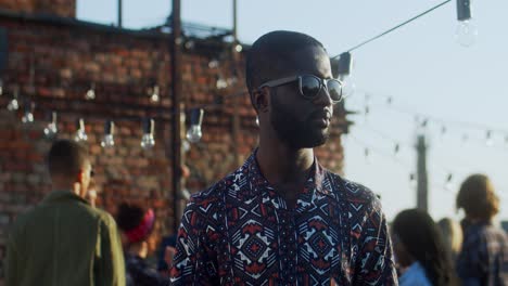 Joven-Con-Gafas-De-Sol-Negras-Mirando-A-Un-Lado-Y-Luego-Girando-La-Cara-Hacia-La-Cámara-Con-Una-Sonrisa-Mientras-Estaba-En-La-Fiesta-De-La-Azotea-Al-Aire-Libre-1